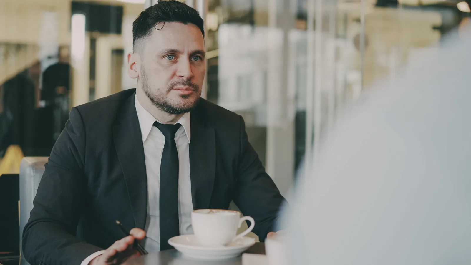 A professional in a suit engaged in a meeting over coffee in a modern café setting.