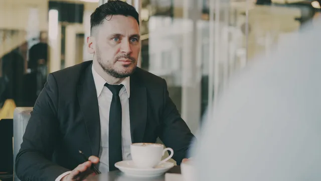 A professional in a suit engaged in a meeting over coffee in a modern café setting. Salarisonderhandeling voorbereiden met marktdata en cao-schalen
